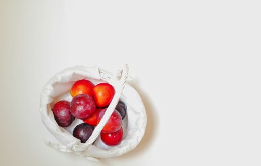 A high angle shot of plums in a small basket on a beige surface
