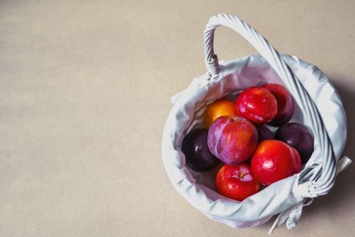 A high angle shot of plums in a small basket on a beige surface