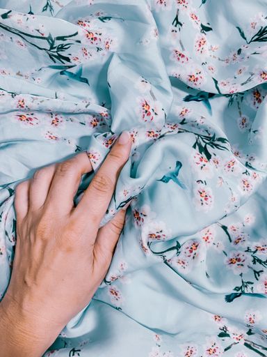 A vertical closeup shot of a person's hand on blue bedsheets with flowers