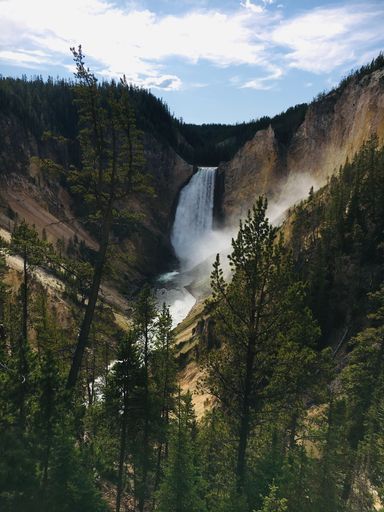 An aerial view of Upper Falls of the Yellowstone River waterfall flowing through lush green mountain forests