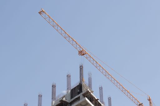 A low angle shot of a tall yellow crane over a building under construction
