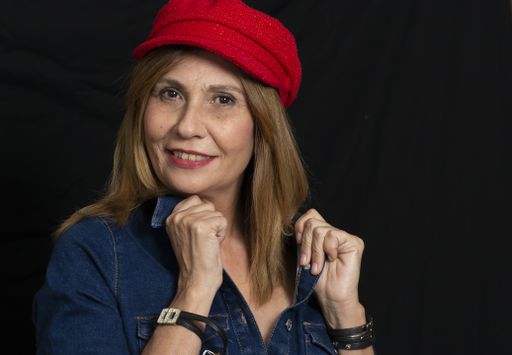 A closeup of a Hispanic woman wearing a denim dress and a red hat in front of a black background