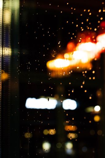 A vertical closeup shot of a window with blurred orange and blue city lights behind it at night