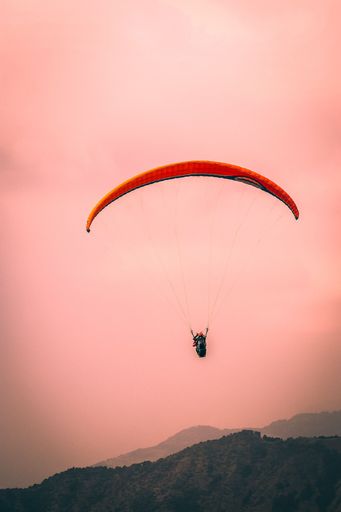 A vertical shot of a person in a red parachute over mountains at sunset