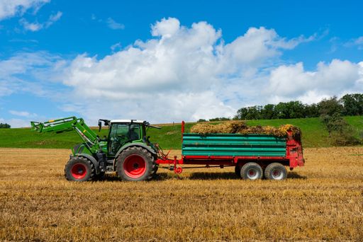 An agricultural combine, hauling a full hay wagon through a grassy field