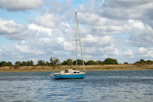 A sailboat floating on a river with the cloudy sky in the background