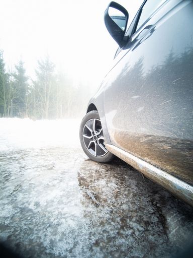 A vertical shot of an electric car parked on a frozen puddle in the winter with a white landscape in front of it