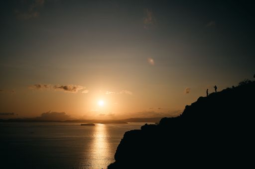 A silhouette shot of hikers on a hill near the sea during a sunset