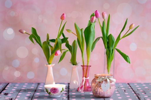 Several vases with delicate ink tulips on wooden floorboards in front of a pink and white spotted wall