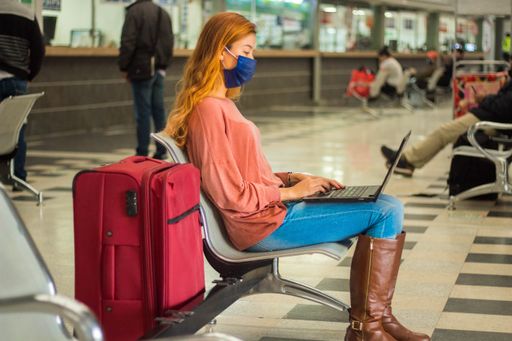 A traveller wearing a mask working on her laptop and waiting for her flight