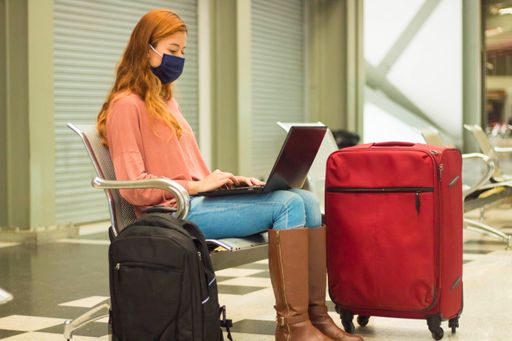 A traveller wearing a mask working on her laptop and waiting for her flight
