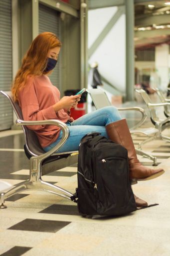 A traveller wearing a mask looking at her phone and waiting for her flight