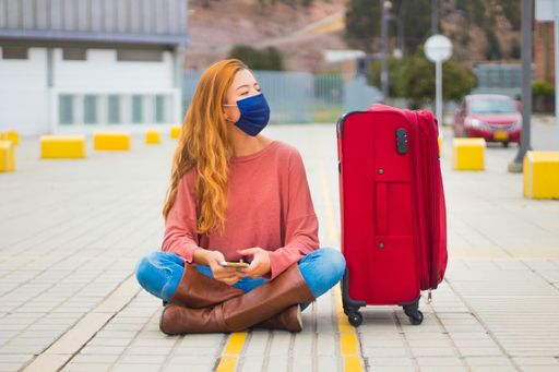 A traveller wearing a mask looking at her phone and waiting for the taxi