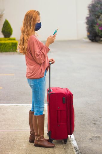 A traveller wearing a mask looking at her phone and waiting for the taxi