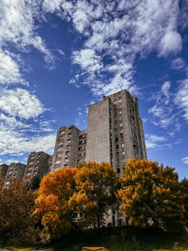 A low-angle shot of residential buildings and trees against a blue cloudy sky