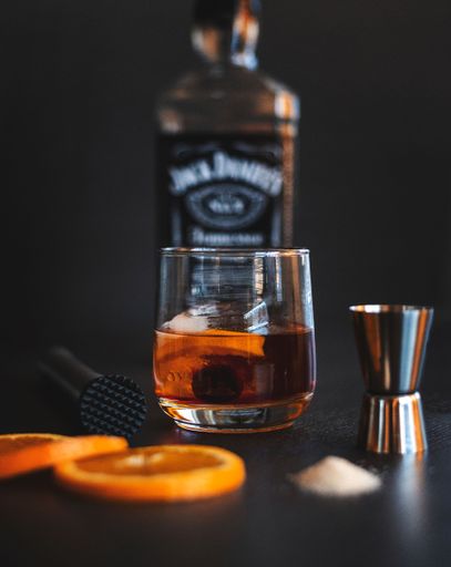 A glass of whiskey with ice and orange slices, along with a bottle of Jack Daniels in the background