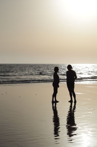 A silhouette of two happy friends standing on the beach reflected on wet sand at sunset