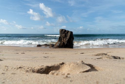 A wave breaks about a rock during a curtain on the sea. Farol da Barra beach, Salvador, Brazil.