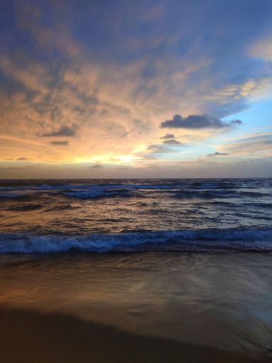 A vertical shot of the sandy beach with waves during the sunset
