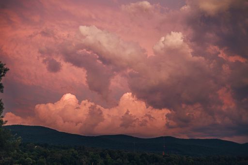 The big white clouds in the pink sunset sky with hill silhouettes underneath