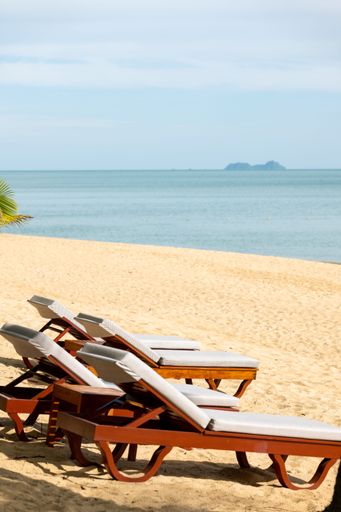 A vertical shot of beach chairs on a sandy coast against a sea in Samui Island, Thailand