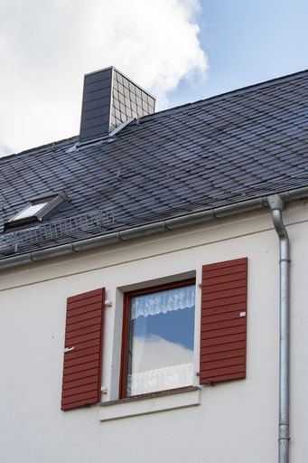 A vertical closeup shot of a classic home with a black roof and a red window