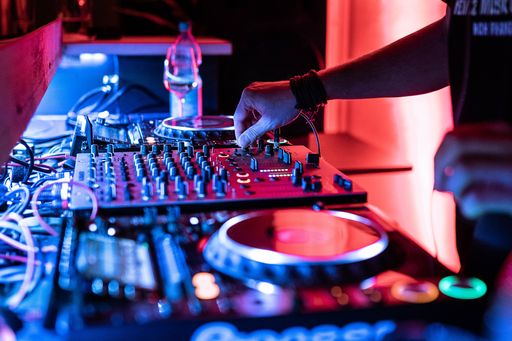 A closeup of DJ hand on a mixing instrument with blue and pink neon lights