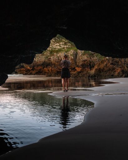 A vertical shot of the Spanish girl from behind standing on the beach visible through the rocks