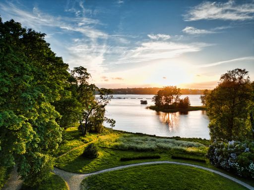 A beautiful scenery of a park with green nature and a lake at bright sunset in the cloudy sky