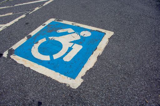 A blue and white marked tarmac sign for disabled persons only parking on asphalt road