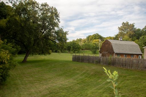 A shed with a fence on a summer day with trees and grass lawn under cloudy sky