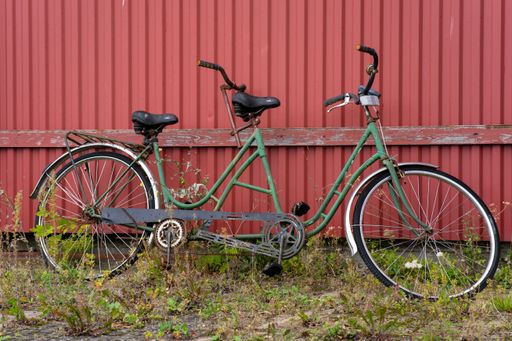 An old green tandem bicycle leaning against a red wall.
