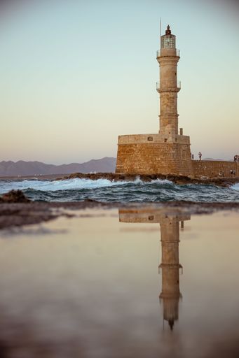 A vertical shot of the Chania Lighthouse in Crete, Greece reflecting on a puddle of water