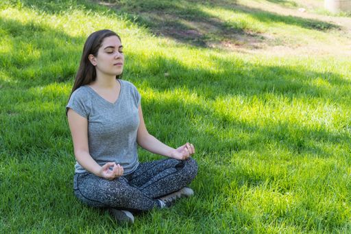 A young caucasian female relaxing practicing yoga sitting on the grass in a public park