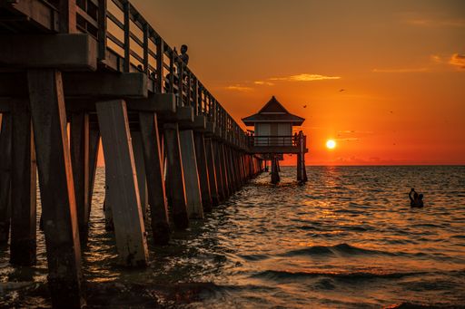 A scenic view of people on a wooden pier in the beautiful Naples beach during a mesmerizing sunset