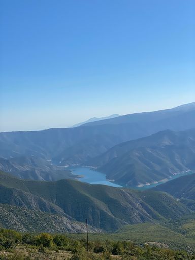 A vertical shot of green hills and river against the background of blue sky.