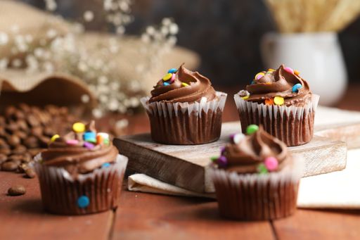 fresh baked chocolate muffins with whipped cream over a wood table with some flowers behind