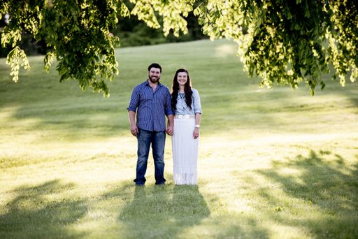 A beautiful shot of a happy couple standing in a grassy field while holdings hands and smiling at the camera