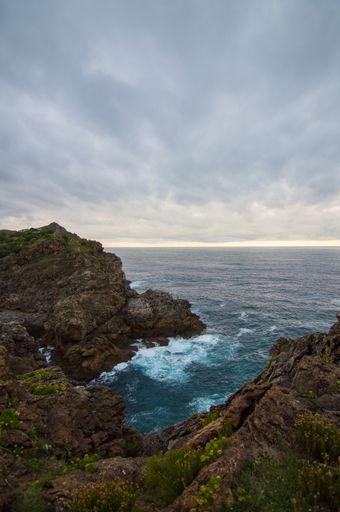 A beautiful scenery of splashing sea waves with rocky cliffs under a cloudy sky