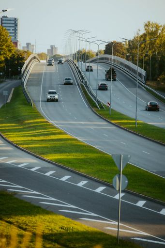 A vertical top view of cars driving along a highway road in the evening time under a sunny blue sky