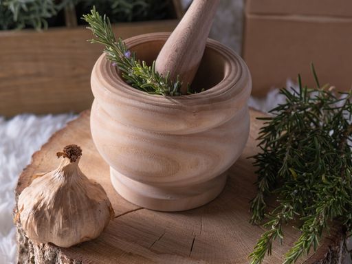 A mortar and pestle with rosemary and garlic on a wooden stump