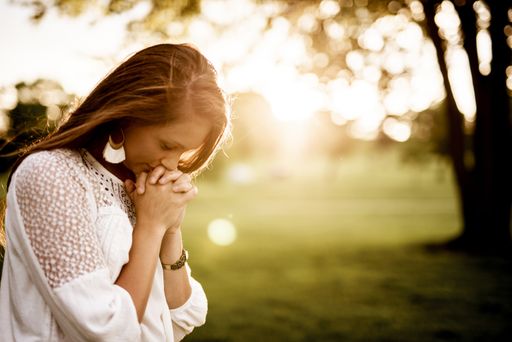 A closeup shot of a female with her eyes closed praying and a blurred background
