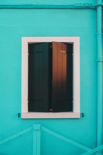 A vertical shot of a small window with black fences on turquoise painted wall