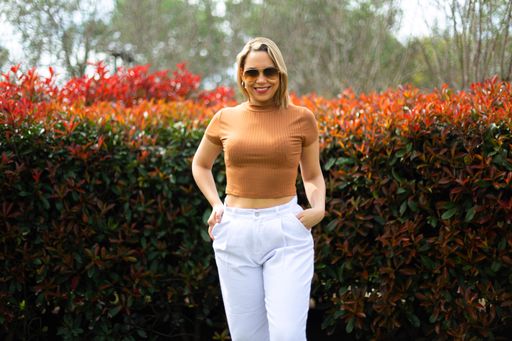 A young Hispanic female in brown top and white pants smiling on camera in the park