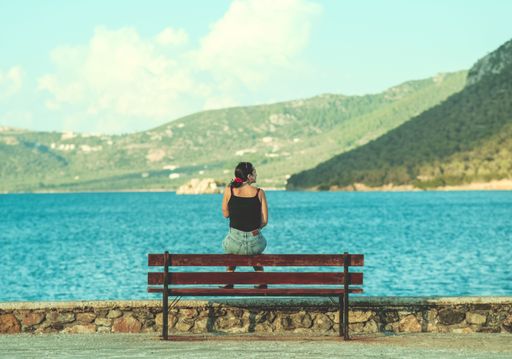 A woman sitting on a bench with a gorgeous view of the sea, daydreaming on a lovely summer day