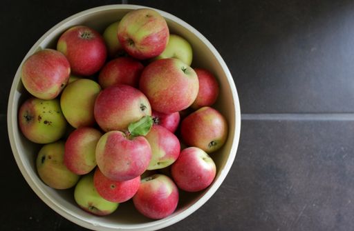An isolated focus horizontal shot of bowl of imperfect green and red apples with holes, harvested from the garden. Basement  tile floor background