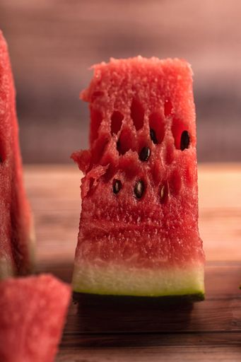 A vertical closeup of red juicy delicious watermelon slice on wooden table