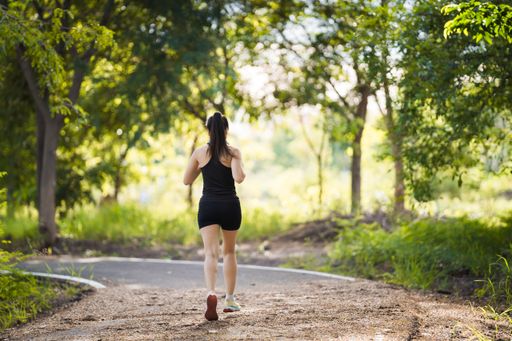 Fit female jogging in a park in black sportswear surrounded by greenery