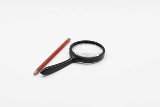 A closeup shot of a magnifying glass and a pencil on a white background