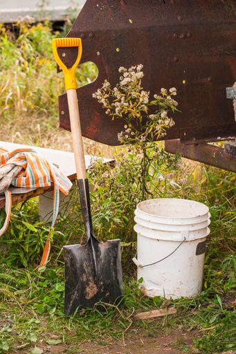 A vertical shot of white bucket and shovel in the soil in the garden
